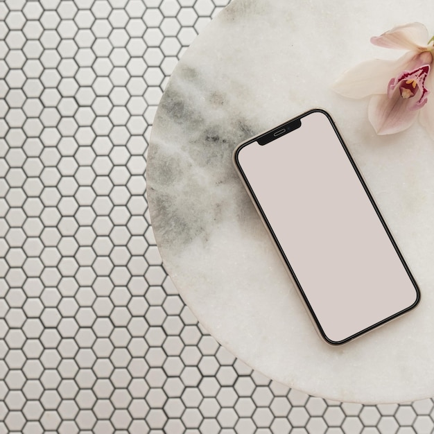 Flatlay of blank clipping path screen mobile phone pink flower on marble stone table on mosaic tile background Aesthetic social media blog template with mockup space Flat lay top view