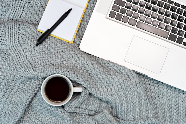 Flatlay del luogo di lavoro accogliente con maglione caldo per caffè, laptop, blocco note. lavoro da casa. scrittura.