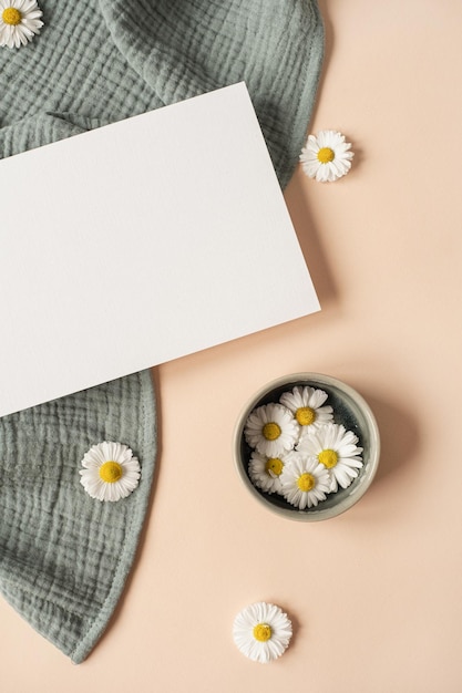 Flatlay esthetische parijse stijl uitnodiging sjabloon blanco vel papier kaart met mockup kopie ruimte kamille bloemknoppen en aquamarijn mousseline doek op neutrale beige achtergrond plat lag bovenaanzicht