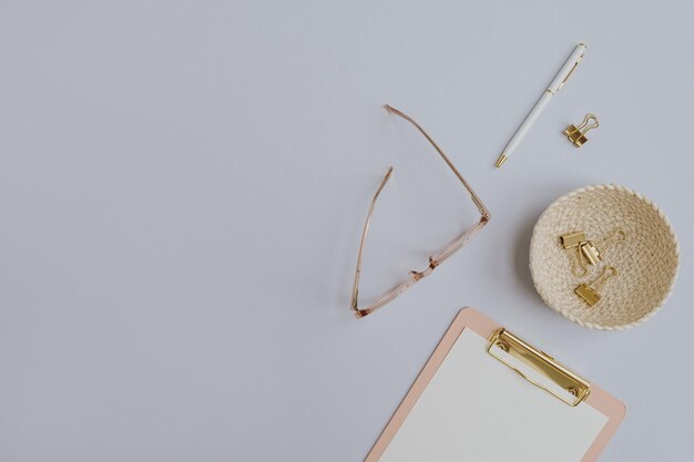 Foto flatlay di accessori femminili d'oro e articoli da ufficio comfortabile spazio di lavoro per l'ufficio a casa lavoro a casa clipboard occhiali clip penna su tavolo pastello flatlay vista superiore