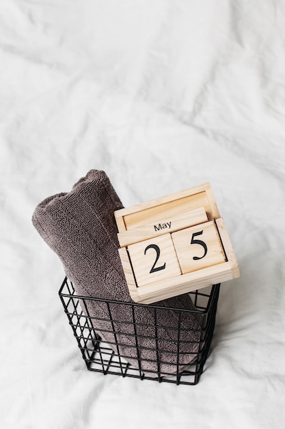 Flatlay gray terry towels on white bedding and a wooden calendar with the date of May 25th