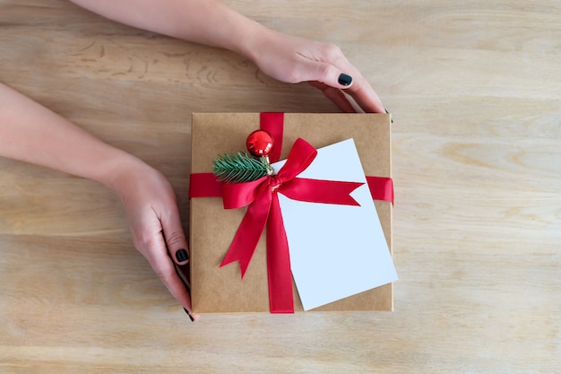 Flatlay holidays giftbox present in woman hands on wooden background for winter holidays, Christmas or New Year