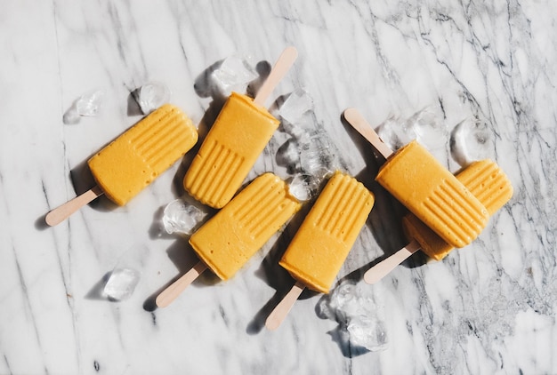 Flatlay of homemade mango smoothie vegan popsicles over marble background