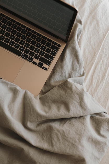 회색 구겨진 침대 시트가 있는 침대에 있는 노트북 컴퓨터의 플랫레이 집에서 프리랜서 개념으로 작업