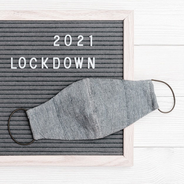 Flatlay letterbord met berichttekst lockdown 2021 en beschermend gezichtsmasker. vergrendel het laadconcept.