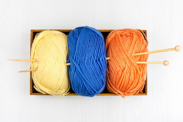 Flatlay of multicolored pastel knitting skeins of yarn and knitting needles on white background