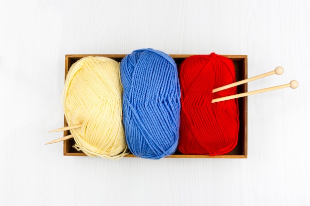 Flatlay of multicolored pastel knitting skeins of yarn and knitting needles on white background