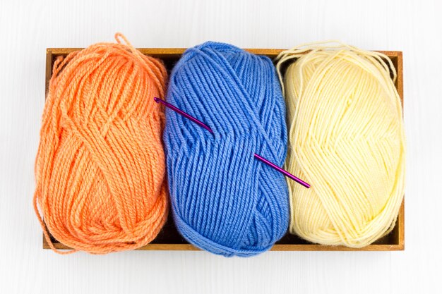 Flatlay of multicolored pastel knitting skeins of yarn and knitting needles on white background