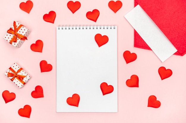 Flatlay notitieblok met een rode envelop met hartjes en cadeautjes op een roze achtergrond. Concept van Valentijnsdag en liefdesbrieven schrijven