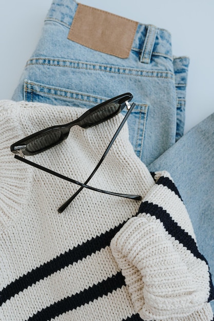 Фото flatlay стильной повседневной женской одежды и аксессуаров эстетическая минимальная модная композиция полосатый свитер синие джинсы солнцезащитные очки flat lay верхний вид