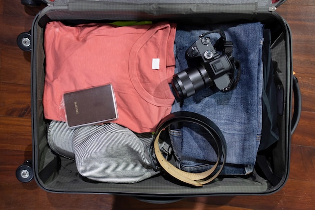 Foto flatlay della macchina fotografica di withclothes della valigia di viaggio aperto e passaporto sui precedenti di legno