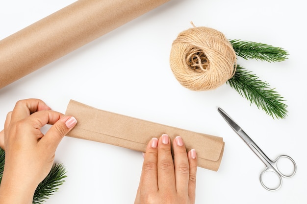 Photo flatlay of process of wrapping christmas gifts in craft wrapping paper with decor of jute rope and f...