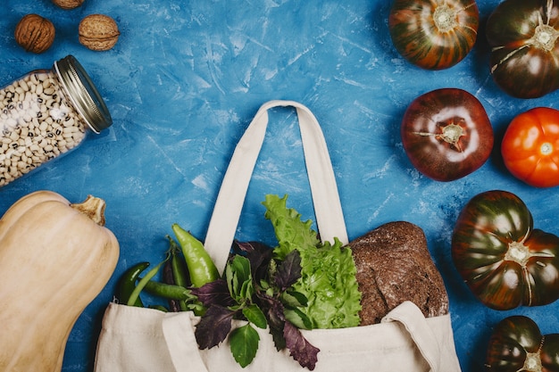 Flatlay of tomatoes, squash pumpkin,  greens and bread in eco bag and beans in a jar