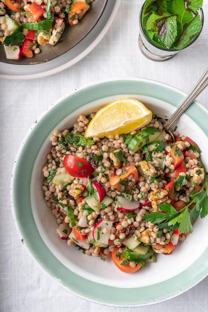 Flatlay of two bowls with healthy vegan wholewheat pearl couscous salad with lemon ad fresh vegetables on a white background with copy space