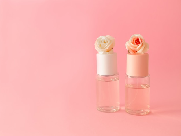 Flatlay van flessen parfum met rozen op roze achtergrond.