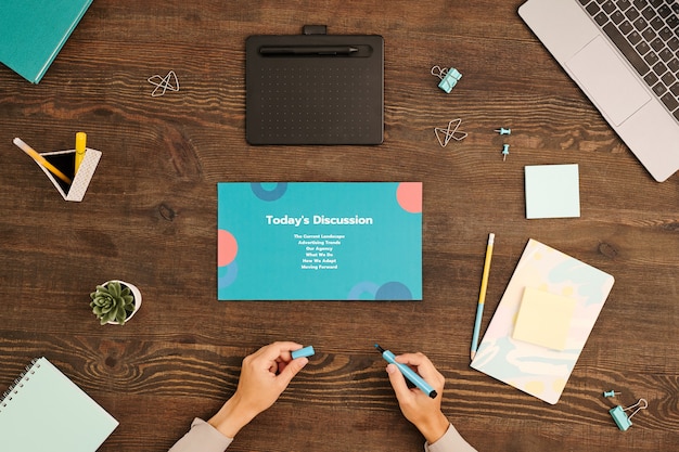 Flatlay van handen van jonge zakenvrouw met blauwe markeerstift die aan een houten tafel zit terwijl ze zich voorbereidt op een werkvergadering met partners