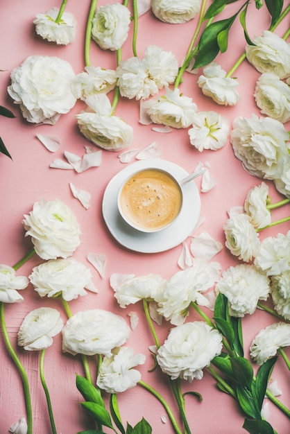 Flatlay van kopje koffie omringd met witte ranonkel bloemen