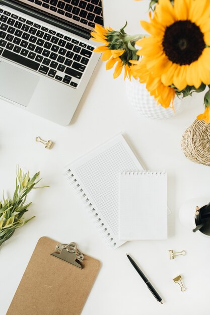 Flatlay van moderne werkruimte met laptop en zonnebloemenboeket op wit