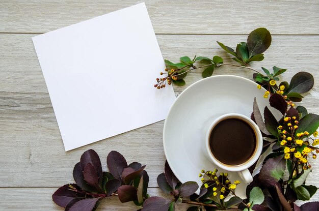 Плоский лист с чашечкой кофе на макете тарелки и белым пустым листом, обрамленным ветвями