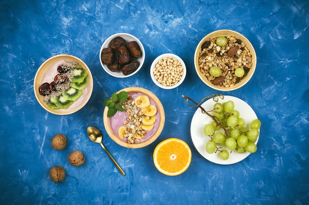 Фото Флэтлай со здоровым веганским завтраком из ягодных растительных мисок для йогурта с мюсли, семенами чиа, различными фруктами и орехами на синем фоне