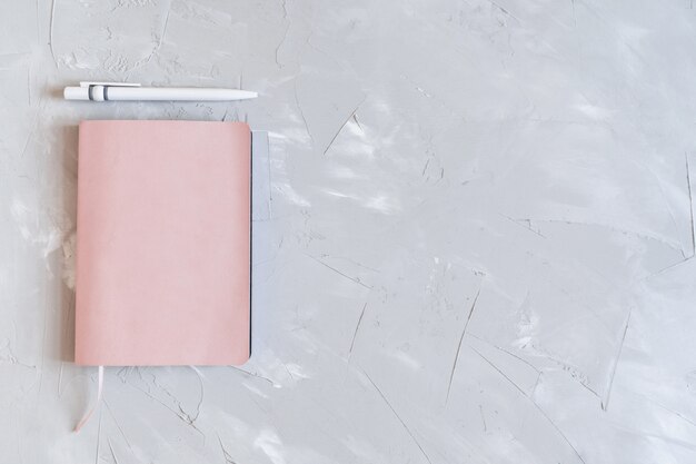 Flatlay with notepad, pen and headphones. Planning your business. Pink notebook on gray background