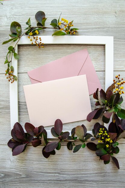 Flatlay with white wooden frame and mockup and copyspace pastel pink envelopes and blank card