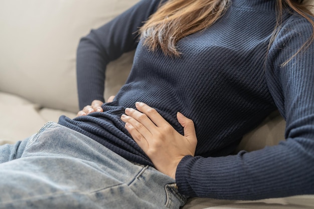 Foto flatulenza asiatica giovane donna ragazza mano nel mal di stomaco soffre di intossicazione alimentare dolore addominale e problemi al colon gastrite o diarrea pancia del paziente addome o concetto di infiammazione