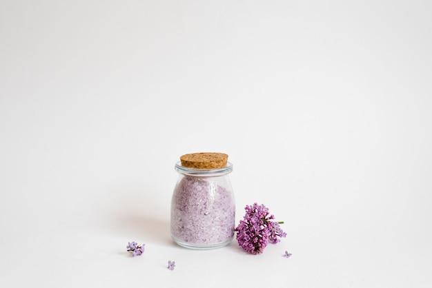 Flavored sea salt with lilac aroma in a glass jar on a light background and flowers Copy space