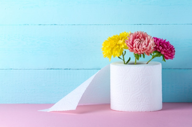 Flavored toilet paper roll and flowers on a pink table. Toilet paper with a smell. Hygiene concept. Toilet paper concept.