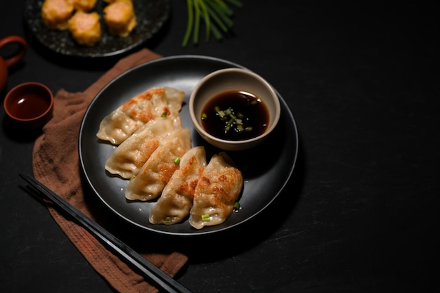 Flavorful Asian Chinese fried dumplings or gyoza with sauce on a black plate and black table