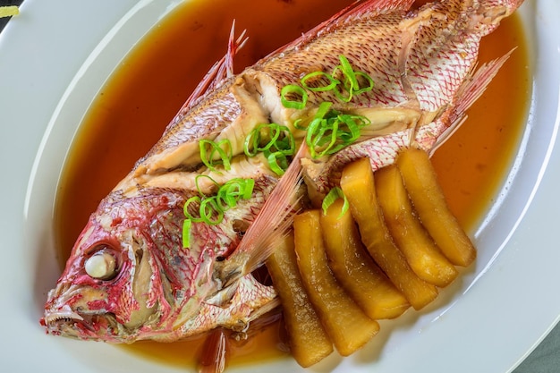 Ароматы моря. Крупный план целой красной рыбы-луциана, приготовленной в имбирно-соевом соусе, на тарелке в 4K