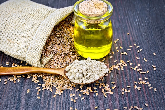 Flax flour in a spoon oil in a glass jar linen seeds in a bag on a dark wooden board background