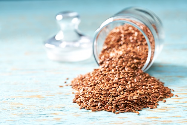 Flax seeds are poured from a glass jar on a blue wooden table