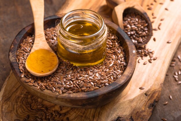 Flax seeds oil and raw seeds on wooden table.