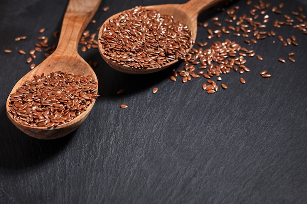 Semi di lino e un cucchiaio di legno su un tavolo scuro. concetto di cibo e bevande sani.