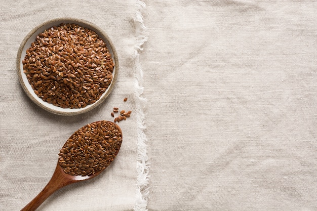 Flax seeds in wooden spoon on natural linen tablecloth. Top view.