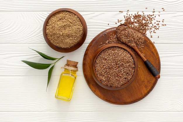 Flaxseeds in a spoon and bowl with a bottle of flaxseed oil and flaxseed flour