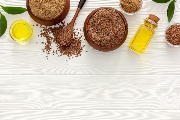 Semi di lino in un cucchiaio e una ciotola con una bottiglia di olio di semi di lino e farina di semi di lino
