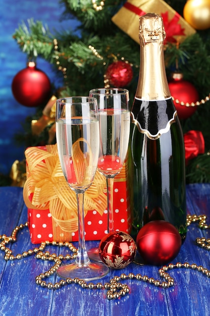 Fles champagne met glazen en kerstballen op houten tafel met kerstboom