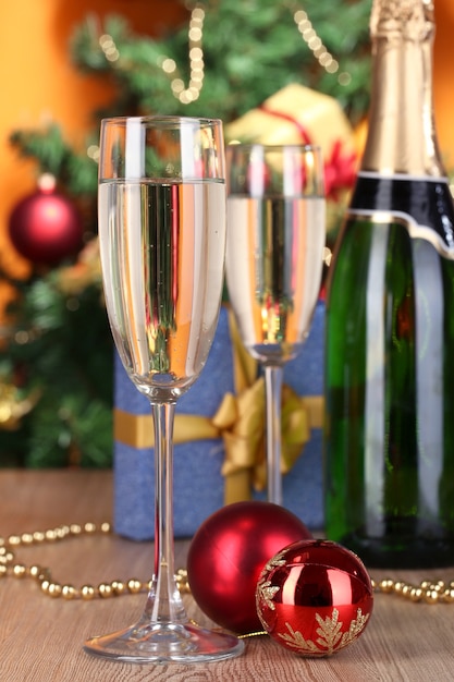 Fles champagne met glazen en kerstballen op houten tafel op kerstboomachtergrond