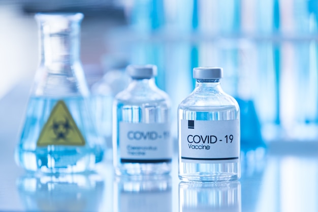 Fles covod-19-vaccinmonster in een laboratorium met laboratoriumapparatuur op onscherpe achtergrond. idee voor onderzoek en laboratoriumtests voor het genezen van coronavirus.