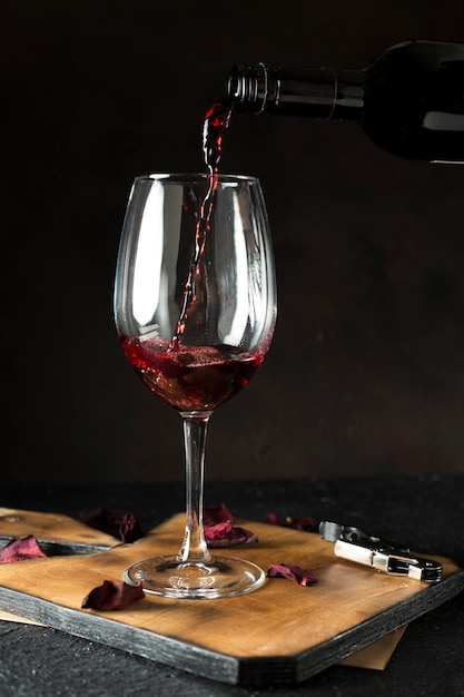 Fles die rode wijn giet in glas op de zwarte achtergrond