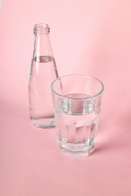 Fles en glas water op roze achtergrond