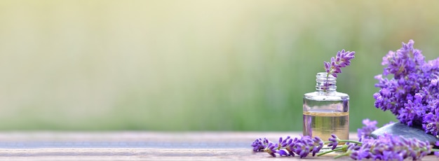 Fles etherische olie en lavendelbloemen op een houten tafel met wazige groene achtergrond