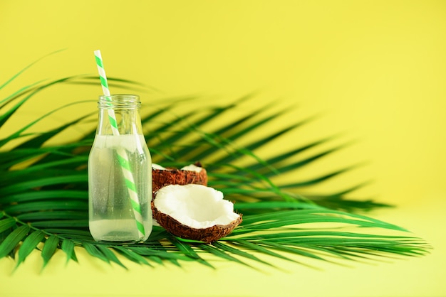 Fles kokoswater en vers rijp fruit. Zomer eten concept. Vegetarisch, veganistisch, detoxdrankje. Kokosnotensap met stro op palmbladen