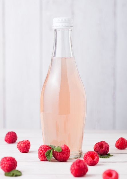 Fles koude frambozen frisdrank met rauwe bessen op lichte houten tafel