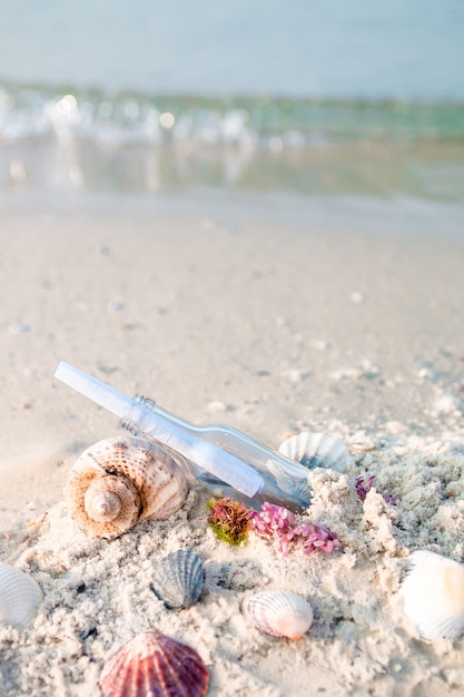 Fles met een bericht of brief op het strand dichtbij zeeschelp