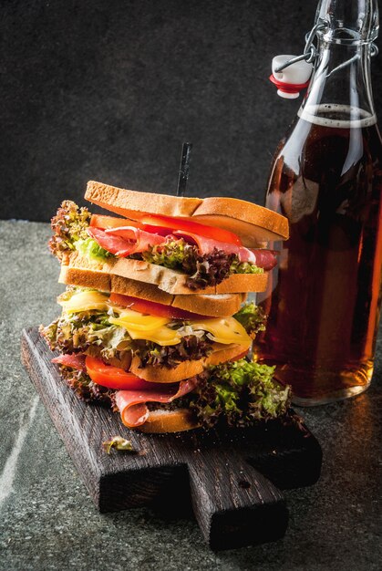 Fles met frisdrank en stapel gezonde broodjes met geroosterd brood, kaas, vlees, groenten en sla