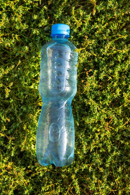 Fles met vers schoon water op groen gras. Bovenaanzicht, kopieer ruimte