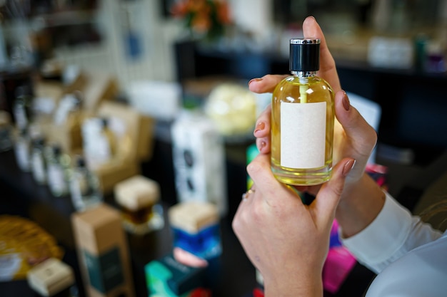 Fles parfum vrouwelijke hand. Jonge vrouw met fles parfum. Modieuze parfums in handen van vrouwen. Meisje spuit parfum. Mooie vrouwenhanden.